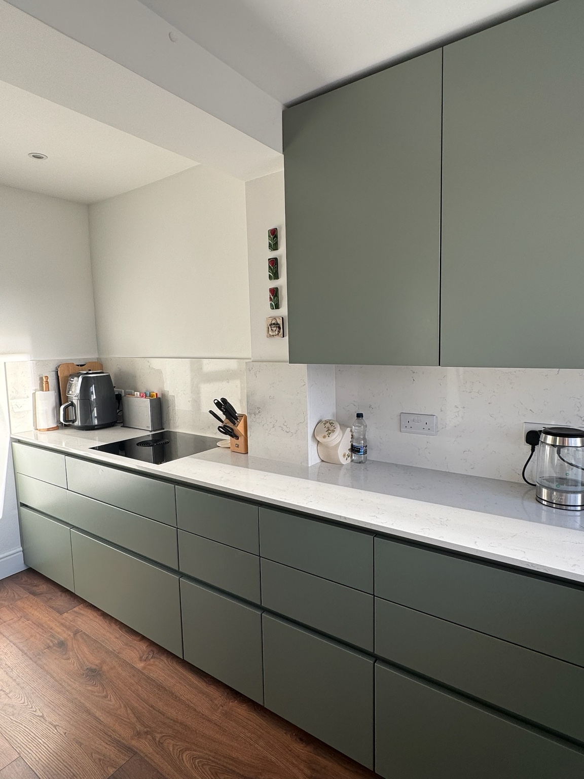 Green handleless kitchen cabinets with a pale worktop and splashback